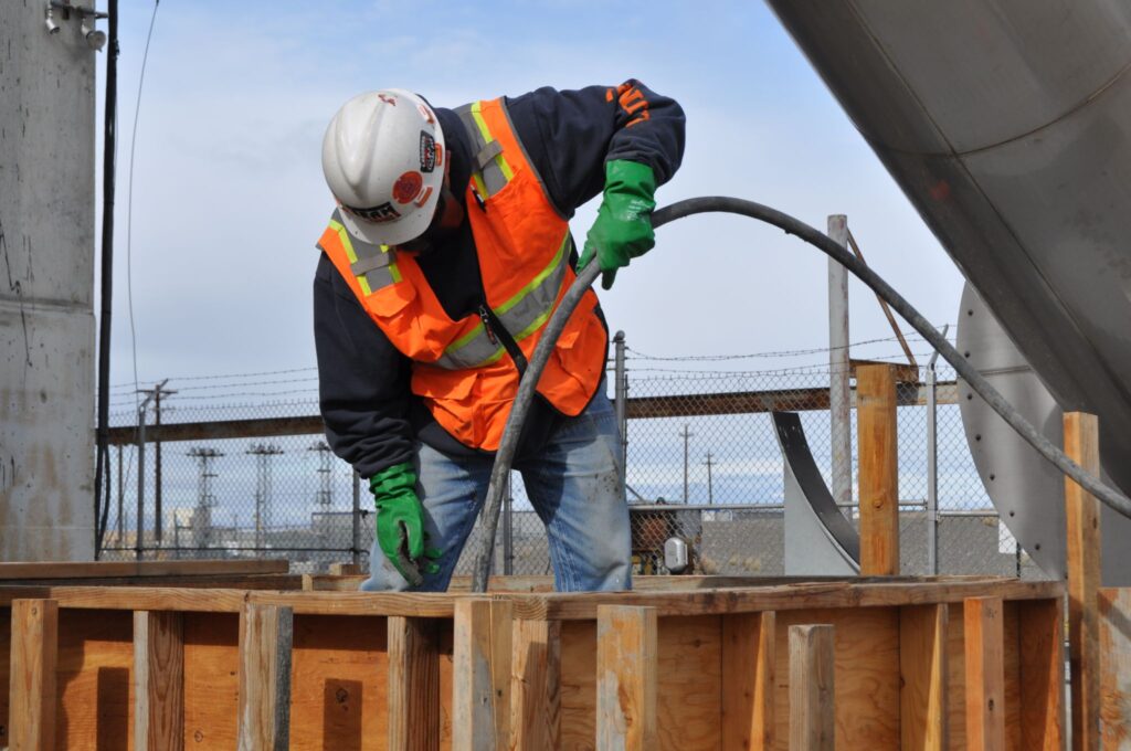 A worker wearing a hard hat, orange safety vest and gloves uses a long tube as part of installation efforts for a new ventilation system. 