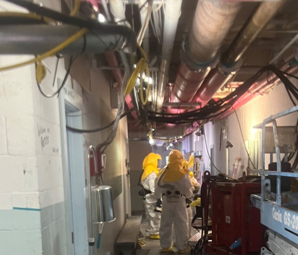 Workers wearing full PPE suits working on demolition inside a building.